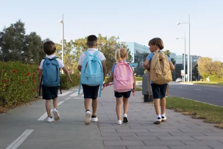 4 enfants marchent sur le trottoir, sac d'école au dos