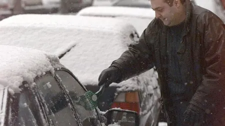 image d'un homme grattant la neige sur son pare-brise